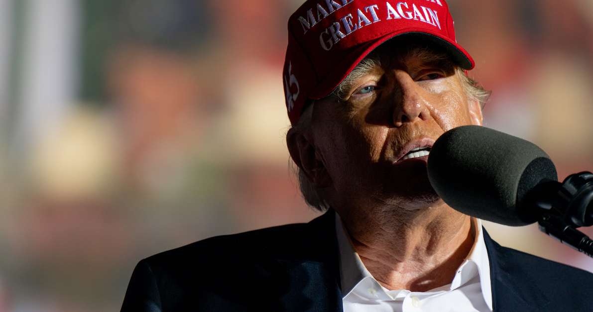 A photo shows Donald Trump wearing a MAGA hat during a speech.