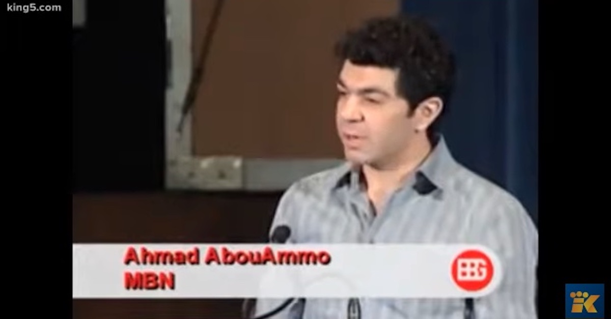 Ahmad Abouammo, wearing a gray striped collared shirt, is speaking into a microphone. He has short black curly hair. 
