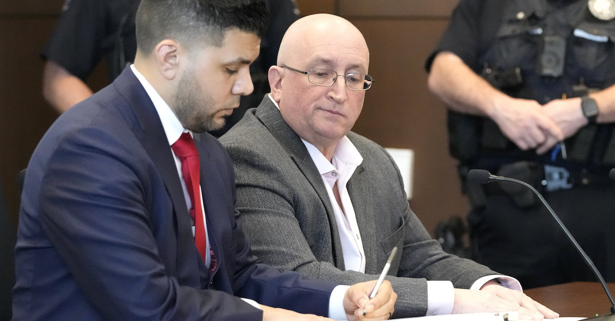 Robert Crimo Jr., wearing an unbuttoned white collared shirt and gray suit coat, looks over his right arm as his lawyer George Gomez takes notes. Gomez is wearing a dark blue suit and red tie.