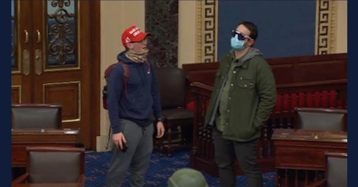 Christopher Carnell is wearing a read "Make America Great Again" baseball cap, a blue hoodie sweatshirt, and a backpack. David Bowman is wearing a green coat, blue face masks, and sunglasses.
